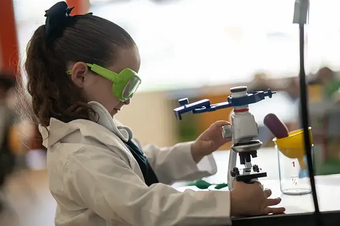 Estudiante realizando experimento con microscopio en laboratorio de ciencias escolares
